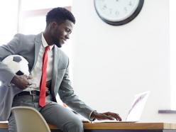 Man holding a soccer ball while using laptop